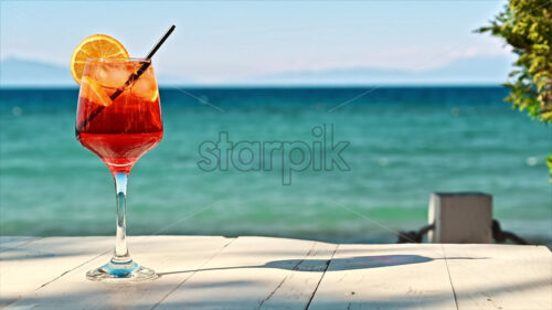 Red cocktail with orange slice on a table by the blue green sea video - Starpik Stock