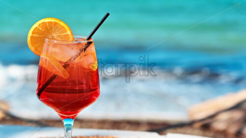 Red cocktail with orange slice on a table by the blue green sea video - Starpik Stock