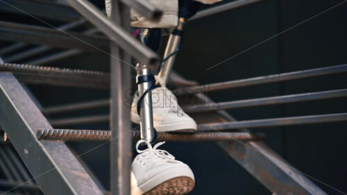 Slow motion view of a man with prosthetic legs and white sneakers going down the metal staircase - Starpik Stock