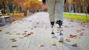 Slow motion view of a man with prosthetic legs and white sneakers. Standing by the fence - Starpik Stock