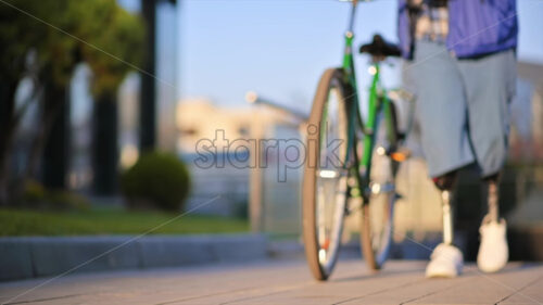 Slow motion view of a man with prosthetic legs. Walking with a bicycle on the street and stops, out of focus effect - Starpik Stock