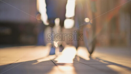 Slow motion view of a man with prosthetic legs. Walking with a bicycle on the street, sunset, out of focus effect - Starpik Stock