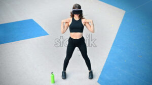 Smiling woman in VR headset in a tracksuit doing exercises on a sports field in a park - Starpik Stock