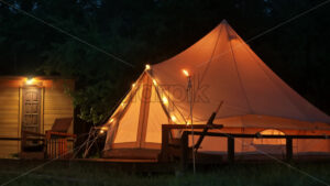 Tent with burning torches, lamps and wooden chairs at glamping, forest around, night - Starpik