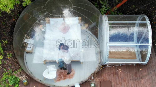 Transparent bubble tent at glamping, Lush forest around and interior. A couple hugging each other and talking - Starpik Stock