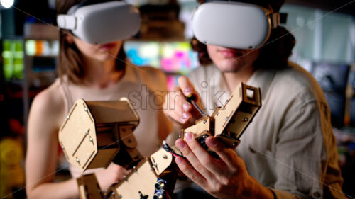 Two young engineers fixing a mechanical robot in the workshop, using VR virtual reality headsets - Starpik Stock