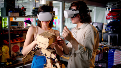 Two young engineers fixing a mechanical robot in the workshop, using VR virtual reality headsets - Starpik Stock