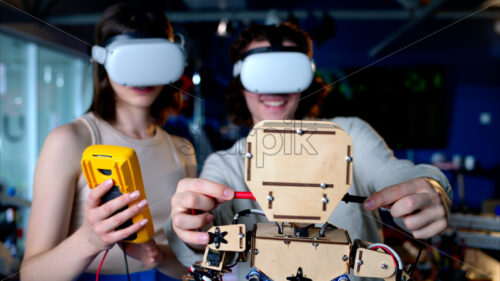 Two young engineers fixing a mechanical robot in the workshop, using VR virtual reality headsets - Starpik Stock