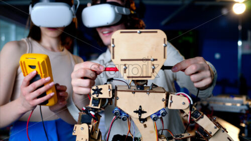 Two young engineers fixing a mechanical robot in the workshop, using VR virtual reality headsets - Starpik Stock