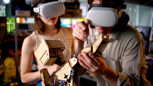 Two young engineers fixing a mechanical robot in the workshop, using VR virtual reality headsets - Starpik Stock