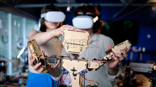 Two young engineers fixing a mechanical robot in the workshop, using VR virtual reality headsets - Starpik Stock