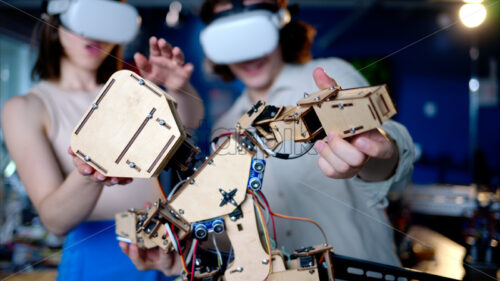 Two young engineers fixing a mechanical robot in the workshop, using VR virtual reality headsets - Starpik Stock