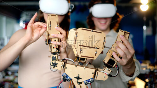 Two young engineers fixing a mechanical robot in the workshop, using VR virtual reality headsets - Starpik Stock