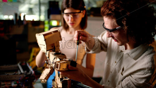 Two young engineers fixing a mechanical robot in the workshop, wearing industrial glasses - Starpik Stock