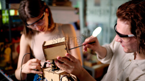 Two young engineers fixing a mechanical robot in the workshop, wearing industrial glasses - Starpik Stock