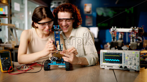 Two young happy engineers fixing a mechanical robot car in the workshop, using VR virtual reality headsets - Starpik Stock