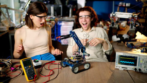 Two young happy engineers fixing a mechanical robot car in the workshop, using VR virtual reality headsets - Starpik Stock