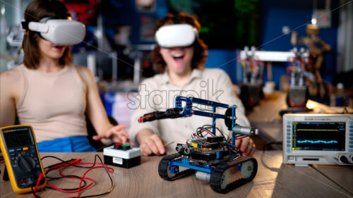 Two young happy engineers fixing a mechanical robot car in the workshop, using VR virtual reality headsets - Starpik Stock