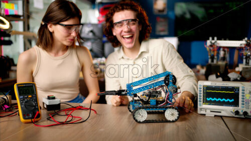 Two young happy engineers fixing a mechanical robot car in the workshop, using VR virtual reality headsets - Starpik Stock