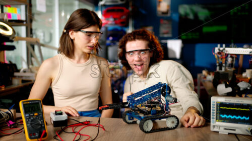 Two young happy engineers fixing a mechanical robot car in the workshop, using VR virtual reality headsets - Starpik Stock