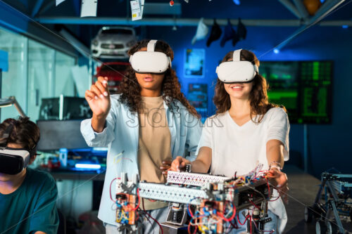 Two young women in VR glasses doing experiments in robotics in a laboratory. Robot on the table - Starpik Stock