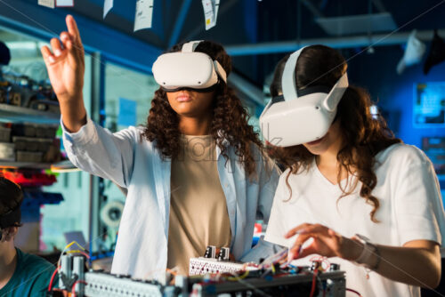 Two young women in VR glasses doing experiments in robotics in a laboratory. Robot on the table - Starpik Stock