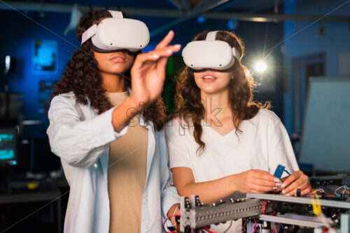 Two young women in VR glasses doing experiments in robotics in a laboratory. Robot on the table - Starpik Stock