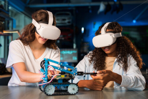 Two young women in VR glasses doing experiments in robotics in a laboratory. Robot on the table - Starpik Stock