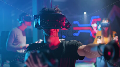 Video – A joyful, interested boy is playing on VR treadmill with helmet, controllers and a backpack. Other people playing nearby, virtual reality - Starpik Stock