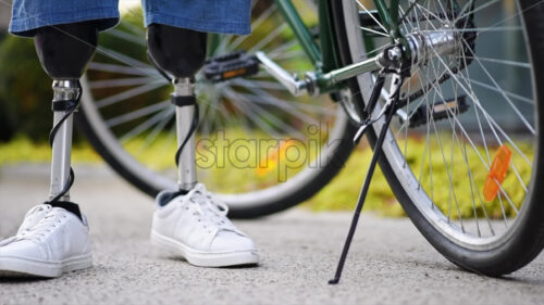 Video – Slow motion view of a man with prosthetic legs. Putting the bike on the kickstand and standing next to it - Starpik Stock