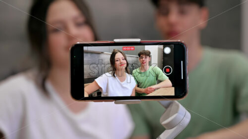 Video – Young smiling man and woman blogger influencers talking and shooting themselves on smartphone on a stabiliser in a kitchen - Starpik Stock