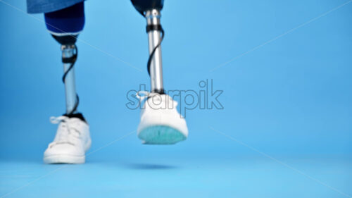 View of a man with prosthetic legs and white sneakers making a step, blue background - Starpik Stock