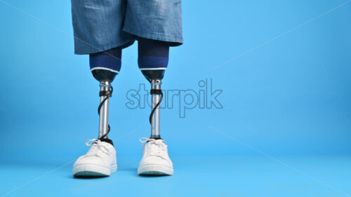 View of a man with prosthetic legs and white sneakers standing against a blue background - Starpik Stock