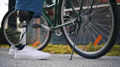 View of a man with prosthetic legs. Putting the bike on the kickstand and standing next to it - Starpik Stock