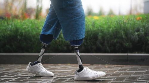 View of a walking man with prosthetic legs and white sneakers at rainy weather, greenery on the background - Starpik Stock