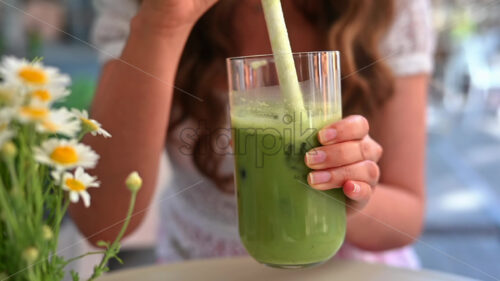 Woman drinking green cold matcha tea with ice at a restaurant terrace - Starpik