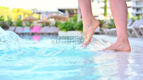 Woman feet making water splashes in a pool, slow motion - Starpik Stock