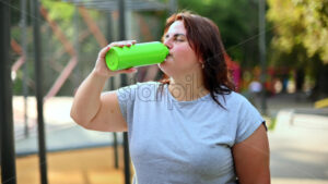 Woman with overweight drinking water on a sports field in a park - Starpik Stock