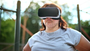 Woman with overweight wearing a virtual reality headset on a sports field in a park - Starpik Stock