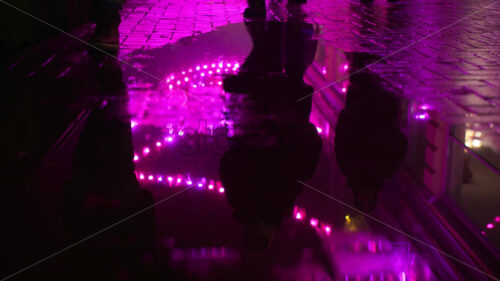 Reflection in rainy water on the ground of people walking on the street at night, in pink light - Starpik Stock