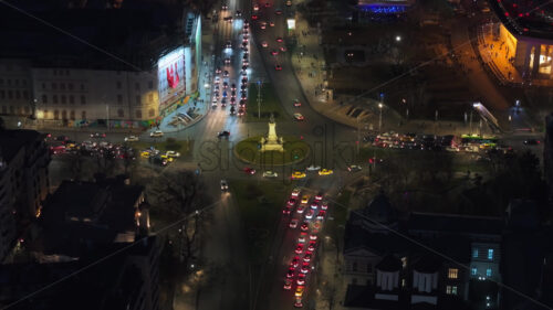 Aerial drone view of a downtown roundabout intersection with moving traffic. Illuminated Bucharest in the night. Romania - Starpik Stock