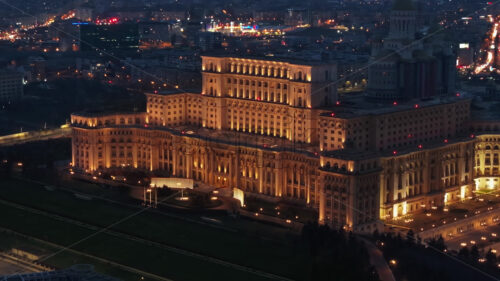 Aerial drone view of illuminated Palace of the Parliament in Bucharest downtown in the evening. Multiple districts around. Romania - Starpik Stock