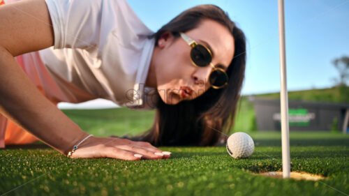 Video Woman trying to push a golf ball into the hole by blowing on it - Starpik Stock