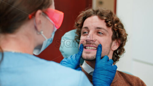 Video Dentist wearing a protective mask, goggles, and gloves checking the teeth of a patient in a dental cabinet