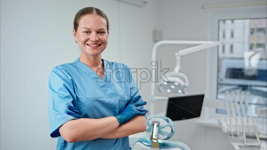 Video Dentist wearing a scrub and standing and smiling in a dental cabinet, in front of a window