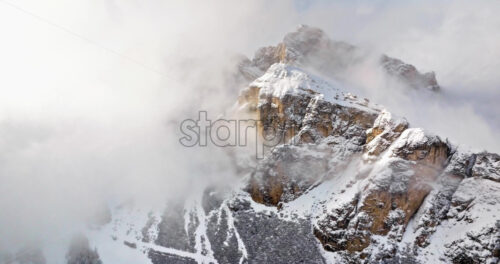 Aerial drone view of snow on the Sassongher mountain in the clouds, in the Dolomites, Italy - Starpik Stock
