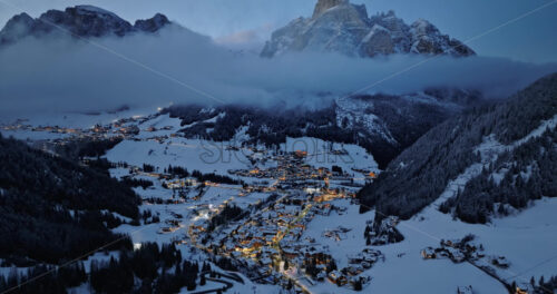 Aerial drone view of the Corvara village covered in snow at blue hour, in South Tyrol, Dolomites, in northern Italy - Starpik Stock