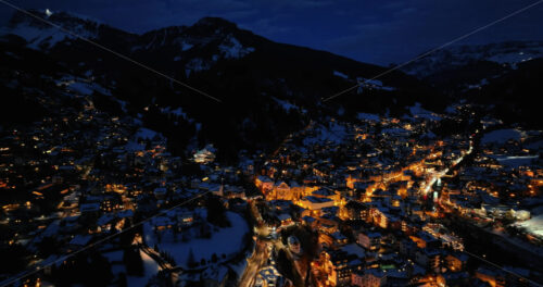 Aerial drone view of the Ortisei town covered in snow at night, within the Dolomites, in northern Italy - Starpik Stock
