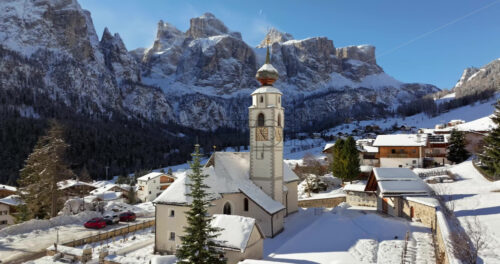 Aerial drone view of the Parrocchia di Colfosco in the Colfosco mountain village covered in snow, in South Tyrol, Dolomites, Northern Italy - Starpik Stock