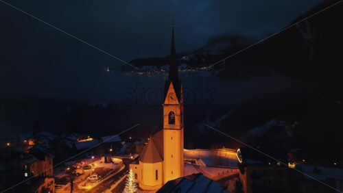 Aerial drone view of the San Lorenzo Church illuminated at night in the Selva di Cadore comune in Dolomites, Italy - Starpik Stock